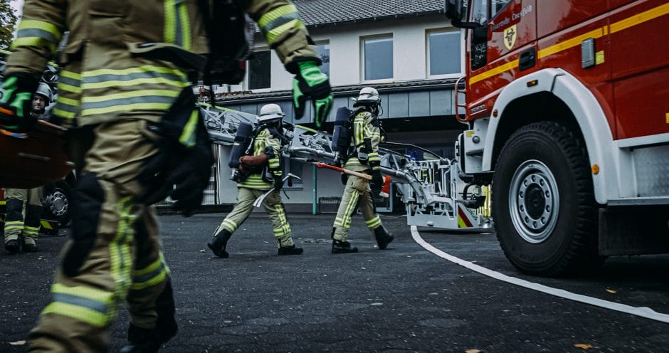 Feuerwehrleute in Einsatzkleidung laufen zu einem Löschfahrzeug während eines Notfalleinsatzes